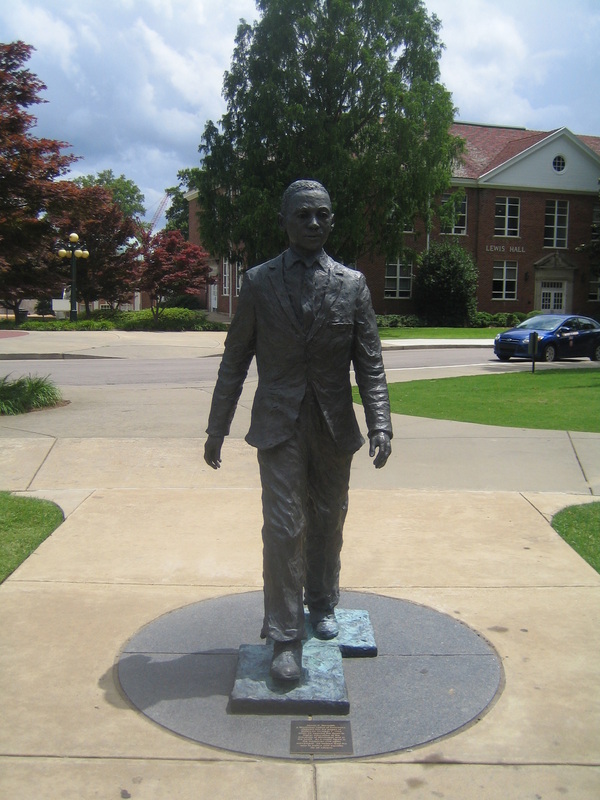 Photograph of James Meredith statue at the University of Mississippi. The statue is made of bronze with two copper plates beneath his feet and in front, a plaque explaining his importance.