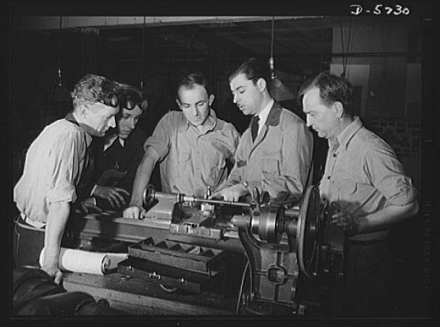 Black and white photograph of students learning by observation in the production of war time equipment.