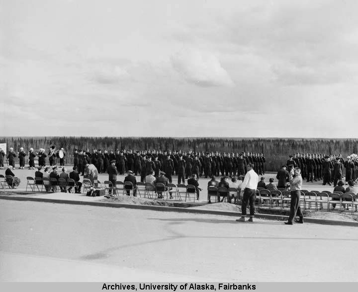Black and white photograph of University of Alaska ROTC students at parade rest during the annual ROTC awards ceremony, with people sitting in front of them in a line, observing.